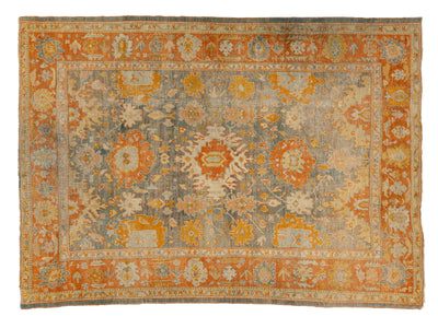 A rectangular antique area rug with a distressed medallion pattern in muted orange, beige, gray, and cream tones, shown flat against a plain white background.