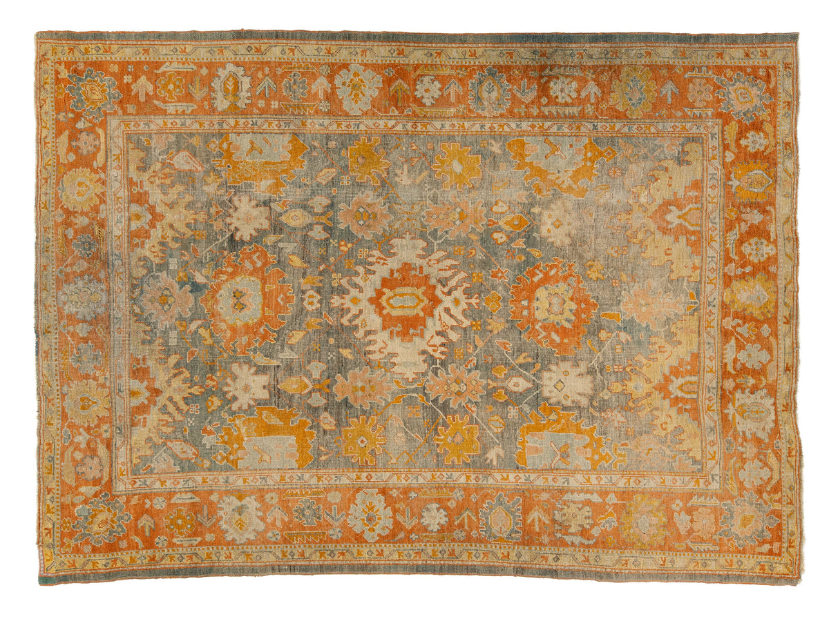 A rectangular antique area rug with a distressed medallion pattern in muted orange, beige, gray, and cream tones, shown flat against a plain white background.