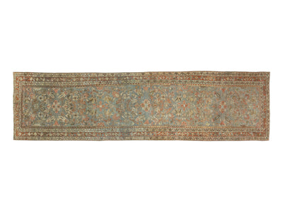 A runner rug with an intricate floral and vine pattern in muted blue, beige, rust orange, and brown tones.
