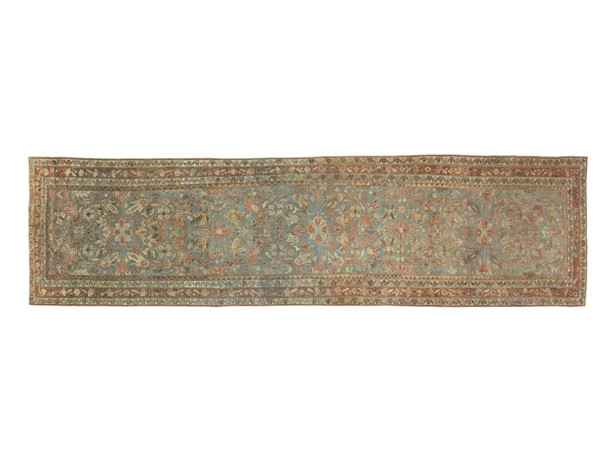 A runner rug with an intricate floral and vine pattern in muted blue, beige, rust orange, and brown tones.