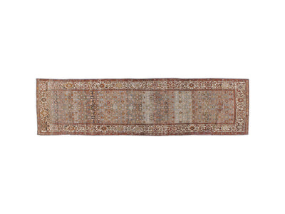 A runner rug with an intricate traditional pattern in muted tones of rust red, beige, gray, and blue, featuring a wide decorative border.