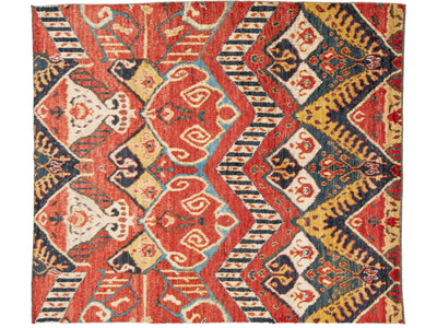 A rectangular area rug with a complex geometric and tribal pattern featuring red, navy blue, cream, and mustard yellow.