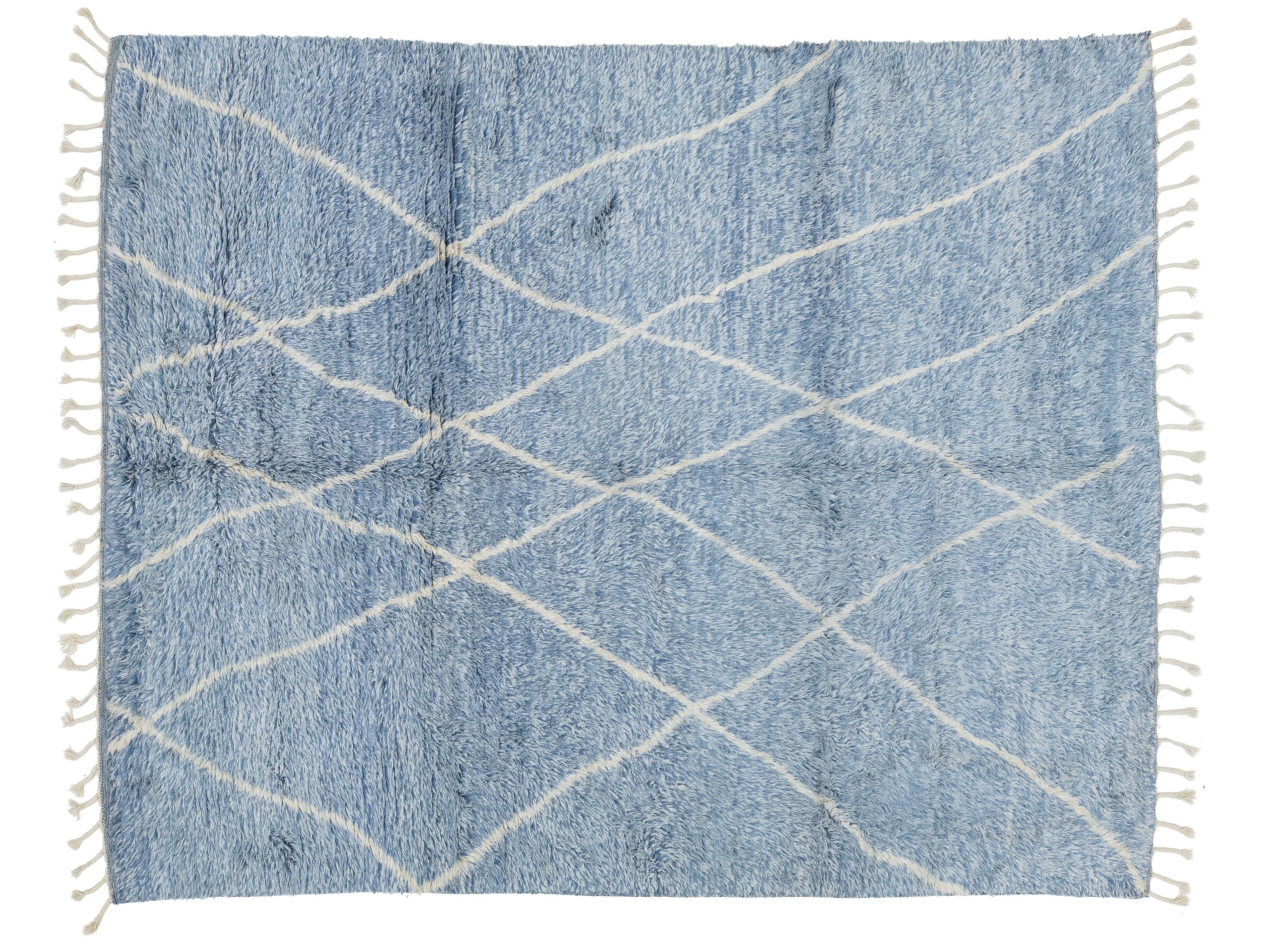 A rectangular blue shag rug with a white geometric crisscross pattern and white fringe tassels on all four sides, shown flat against a white background.