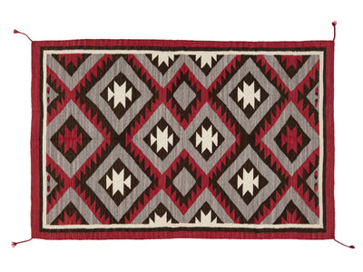 A rectangular woven rug with a Southwestern geometric pattern in red, dark brown, light gray, and off-white, featuring a solid red border and corner tassels on a white background.