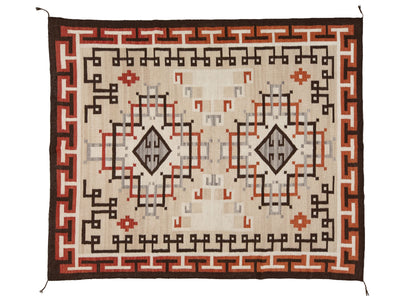 A rectangular woven rug with a Southwestern geometric pattern, featuring a cream center, brown borders, and accents of terracotta red, black, and gray.