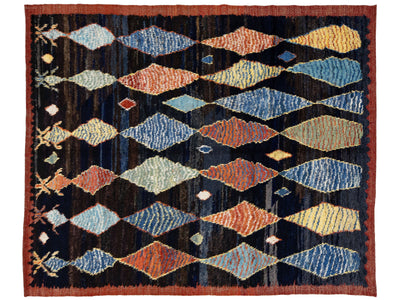 A rectangular woven rug with a dark navy and black background, featuring a repeating pattern of stylized diamond shapes in muted blue, rust orange, beige, and yellow, finished with a rust-colored border.