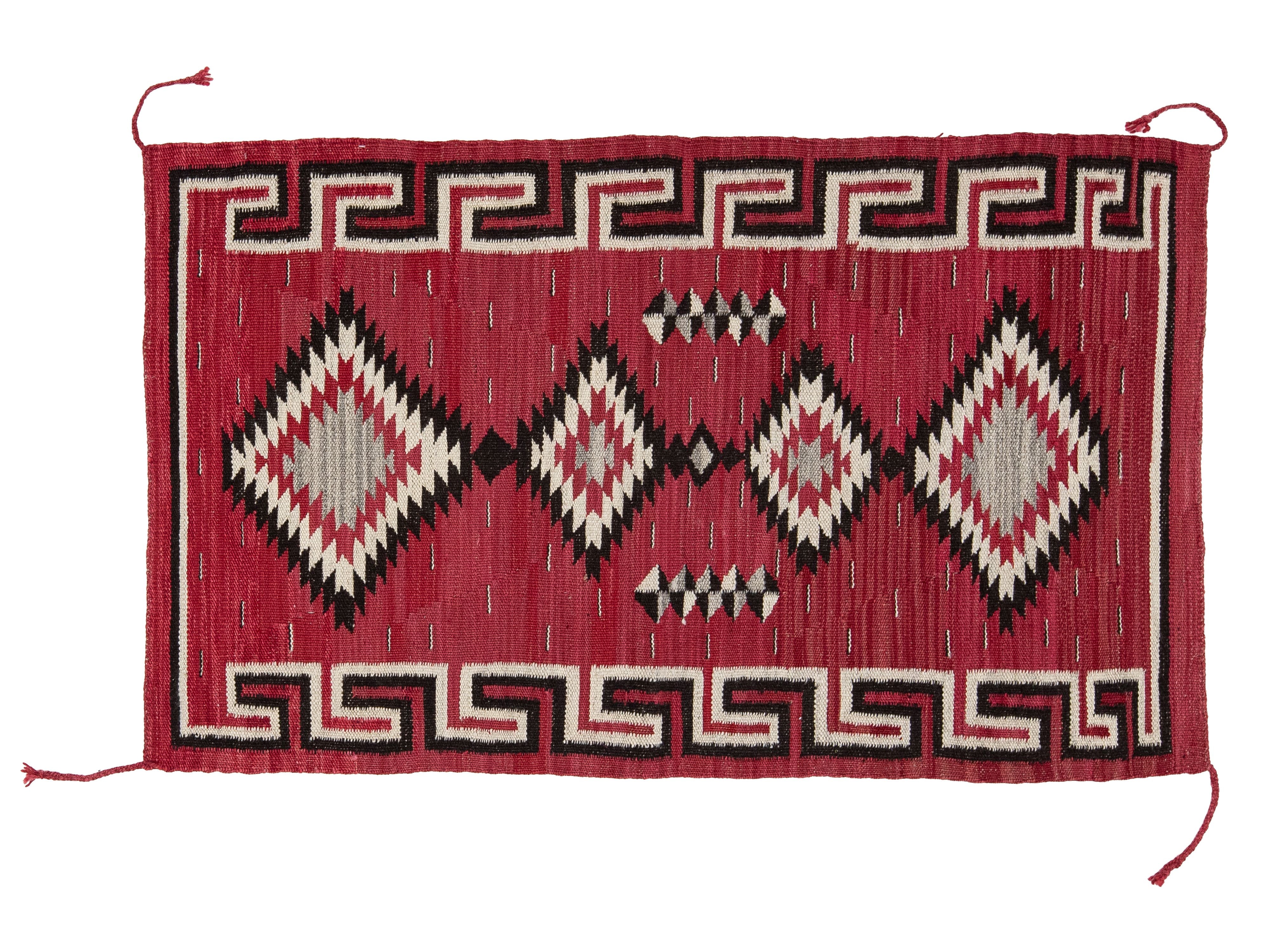 A rectangular woven rug with a red field, featuring large diamond motifs in black, cream, and red, bordered by geometric patterns.