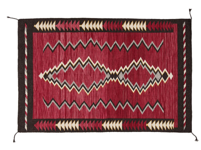 A rectangular woven rug with a deep red center field, black border, and cream and gray geometric zigzag and diamond motifs, shown flat against a white background.