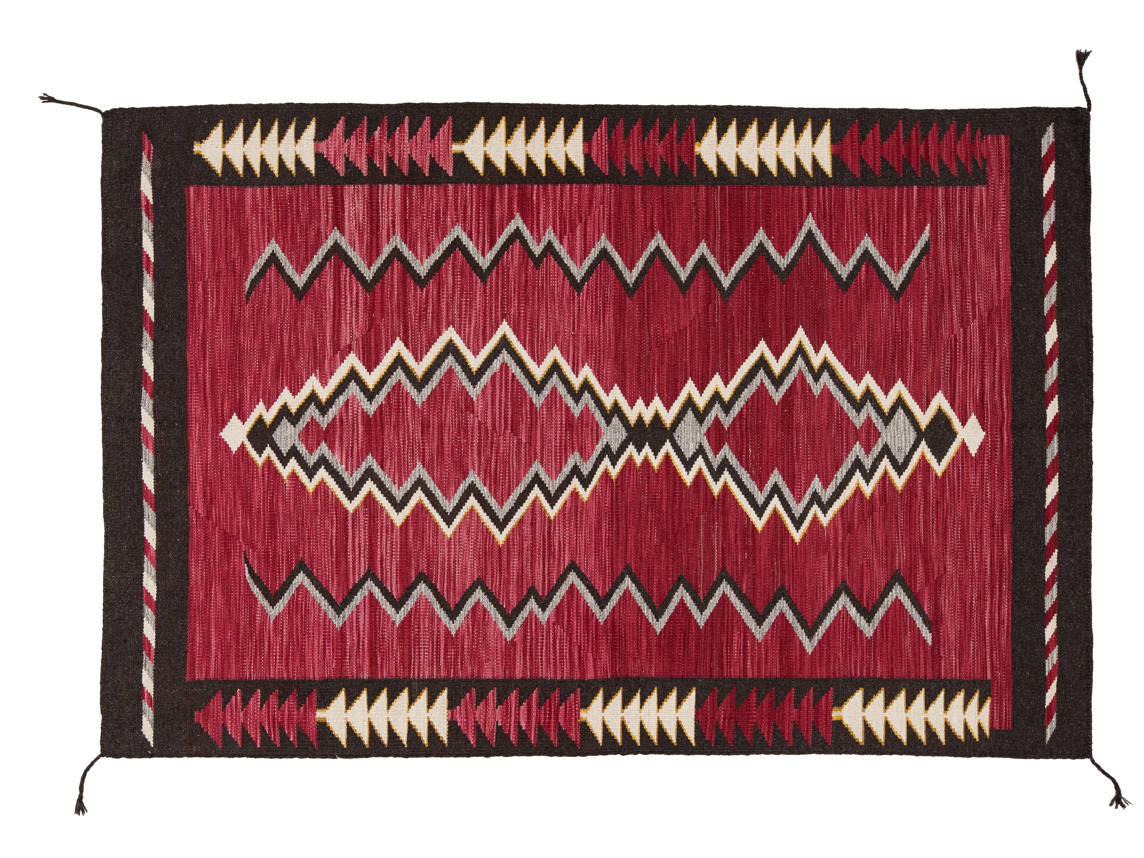 A rectangular woven rug with a deep red center field, black border, and cream and gray geometric zigzag and diamond motifs, shown flat against a white background.
