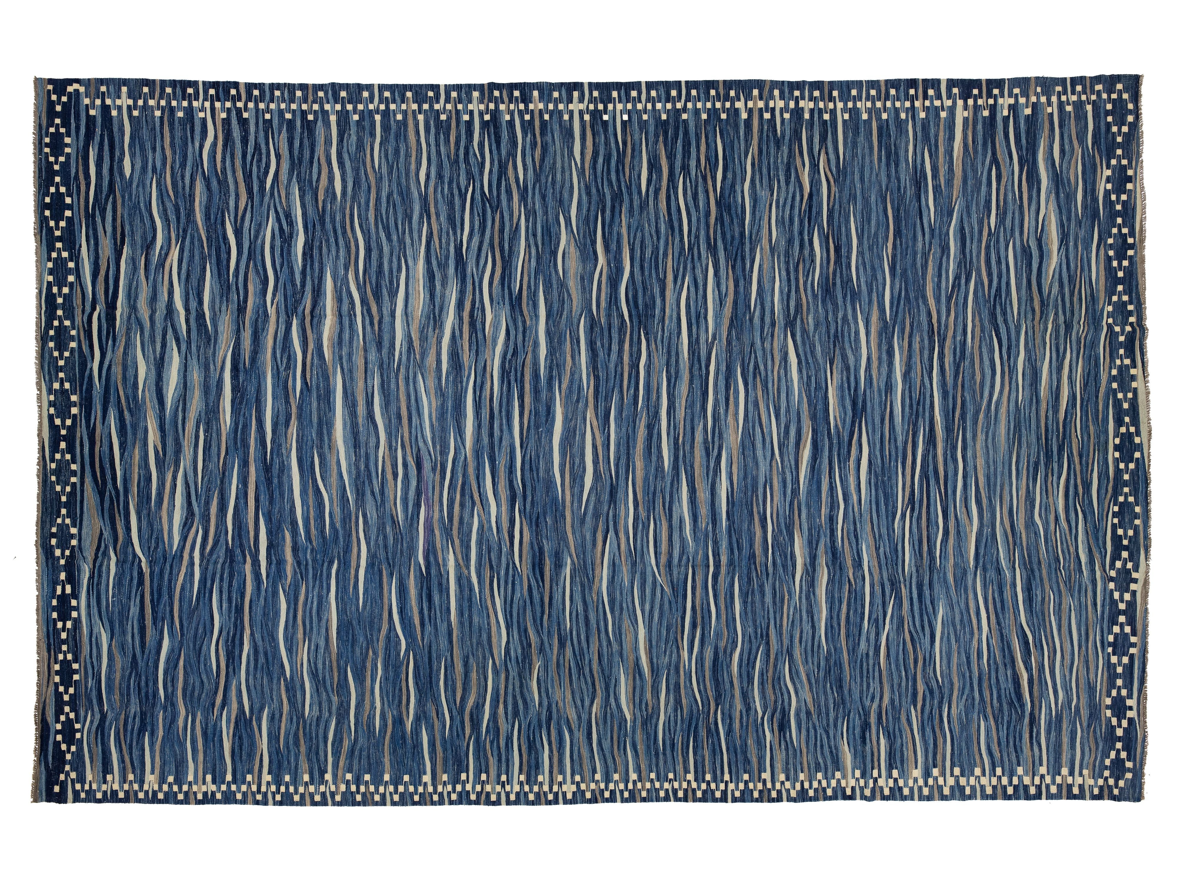 A rectangular area rug with a textured, hand-woven appearance. The design features a dominant medium blue field with vertical wavy lines in cream and beige, framed by a decorative border with small blue and beige dots.