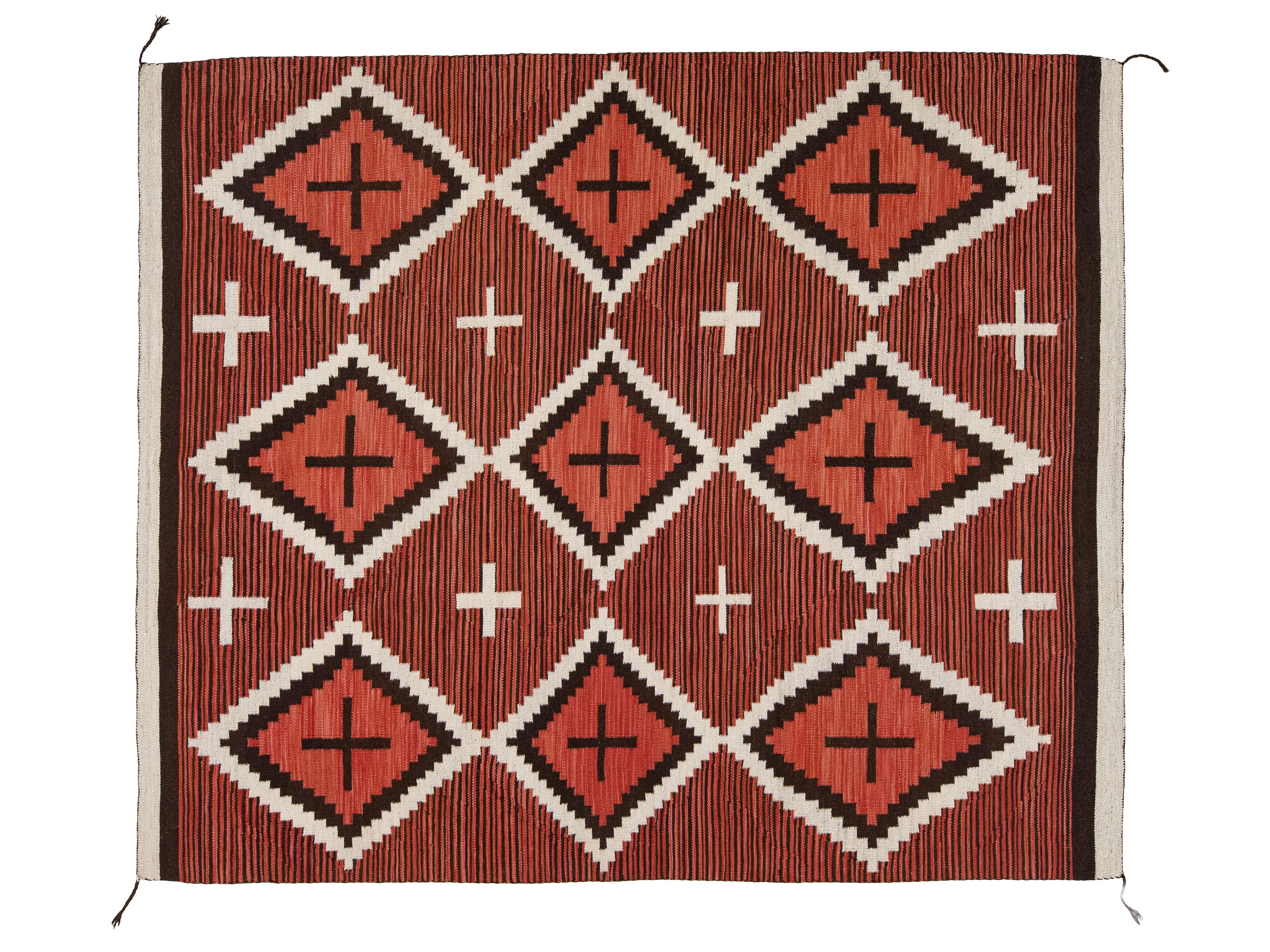 A rectangular woven textile rug or blanket with a geometric Southwestern-style pattern, featuring terracotta red, black, and off-white diamond motifs with cross accents and vertical striped texture.