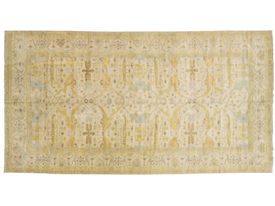 A rectangular oushak-style area rug with an intricate traditional pattern in pale yellow, beige, and light blue, shown flat against a white background.