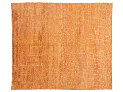 A rectangular area rug with a textured, woven surface in a warm orange and peach color palette, featuring subtle tonal variations and a subtle grid-like pattern.