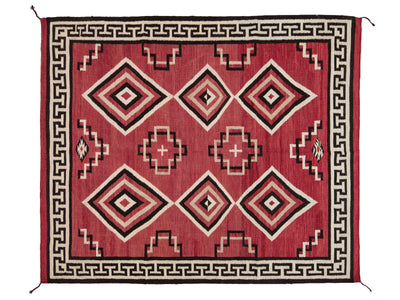 A rectangular woven rug with a red field, black and cream geometric diamond motifs, and a black Greek key border.