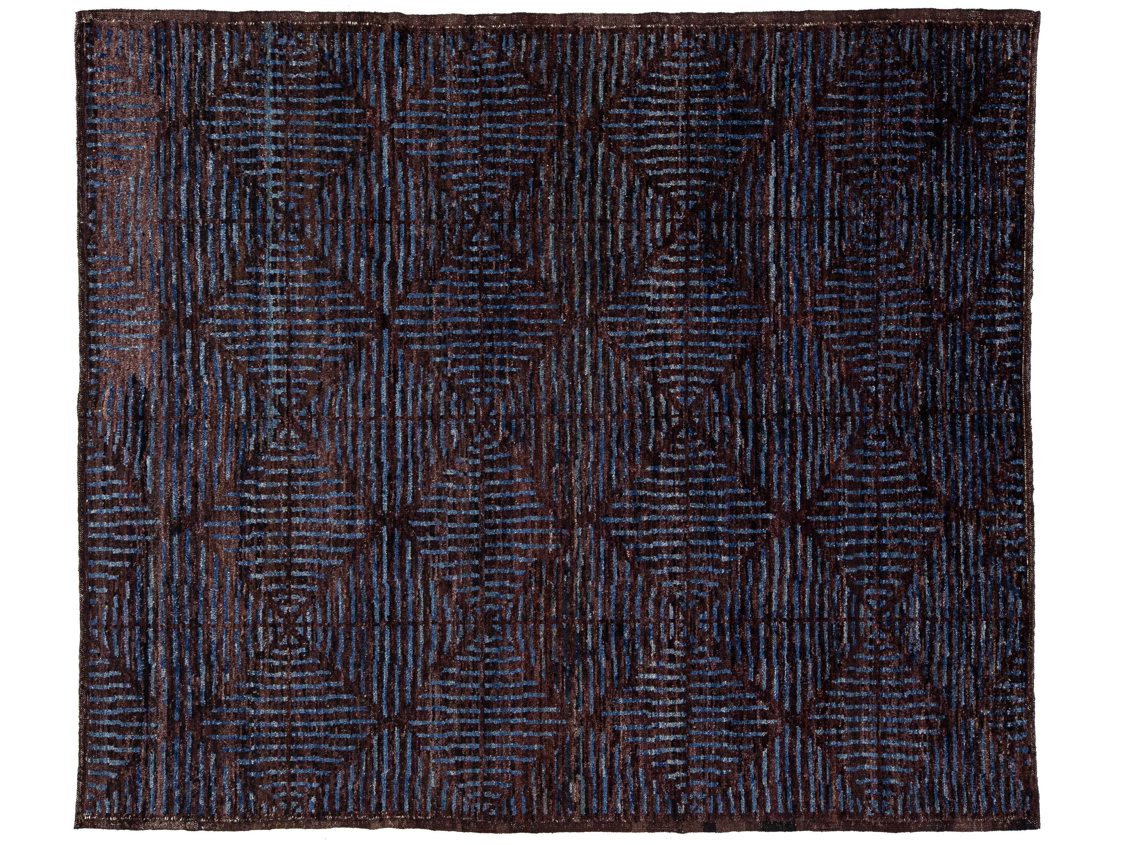 A rectangular area rug with a dark navy and brown geometric diamond pattern, featuring a textured, hand-woven appearance.