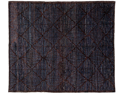 A rectangular area rug with a dark navy and brown geometric diamond pattern, featuring a textured, hand-woven appearance.