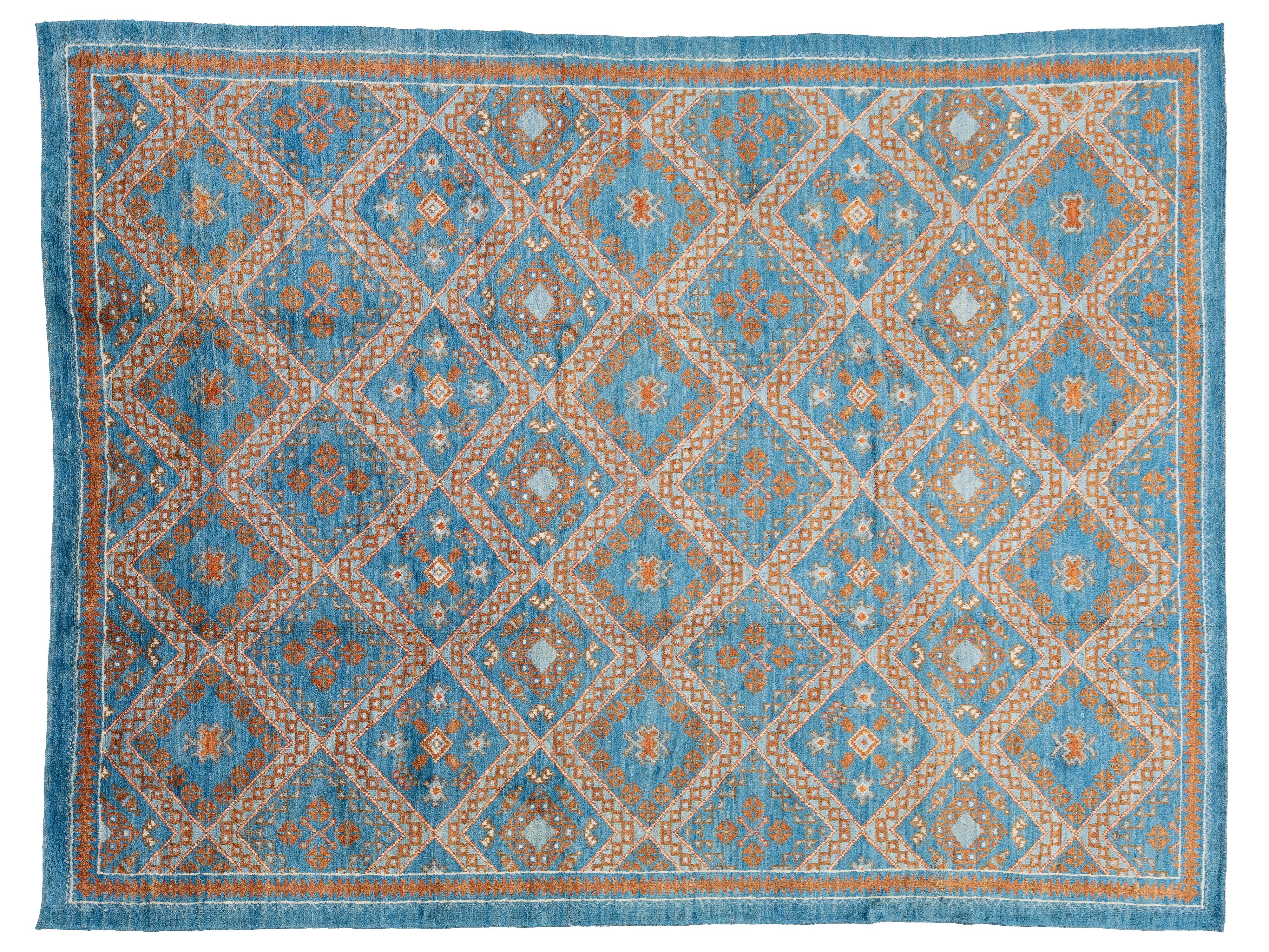 A rectangular area rug with a geometric diamond pattern in shades of blue, beige, and rust orange, finished with a matching blue border.