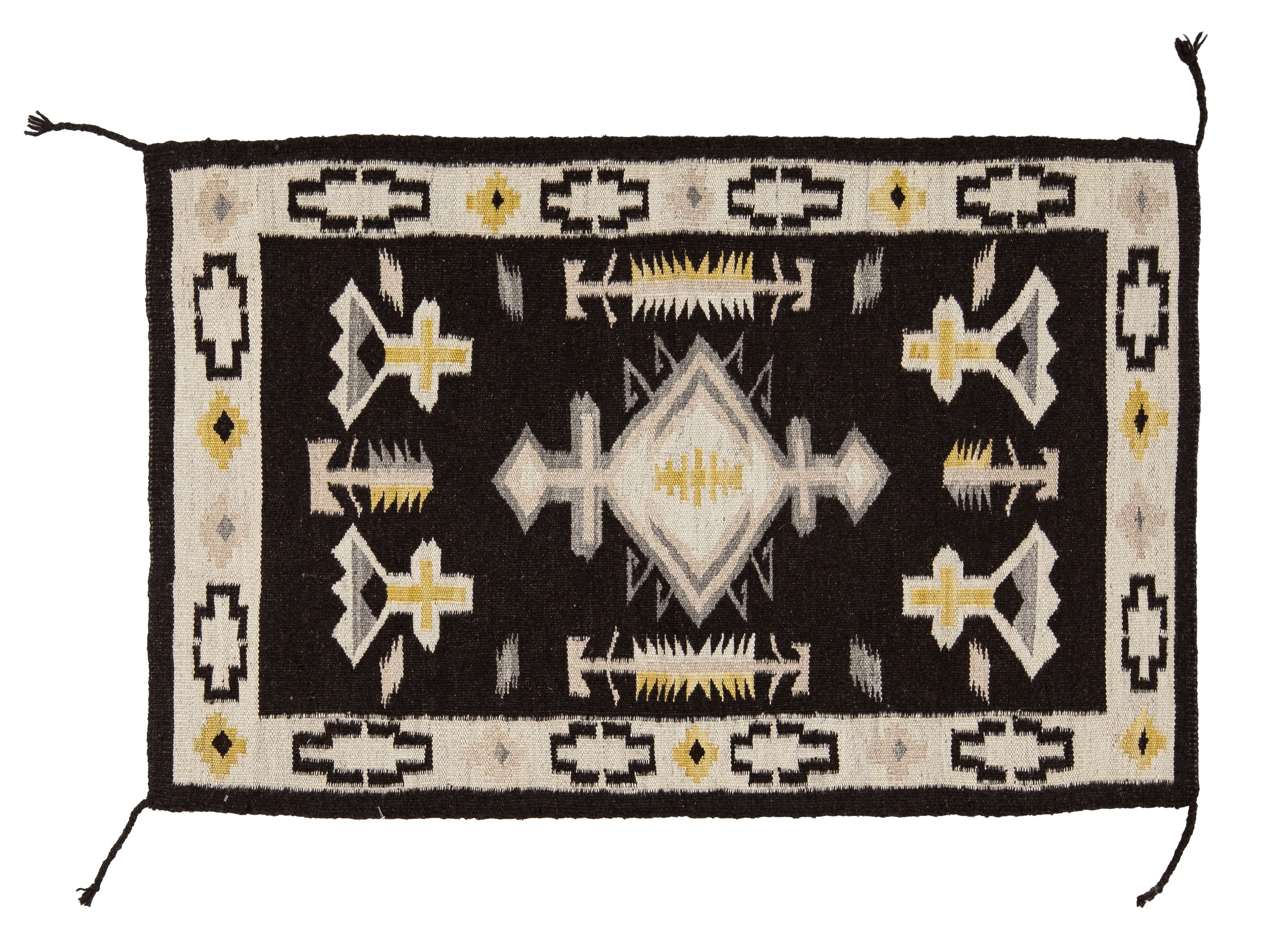 A rectangular Southwestern-style woven rug with a black center field, cream border, and geometric motifs including diamonds, crosses, and fish-like symbols in black, cream, gray, and mustard yellow.