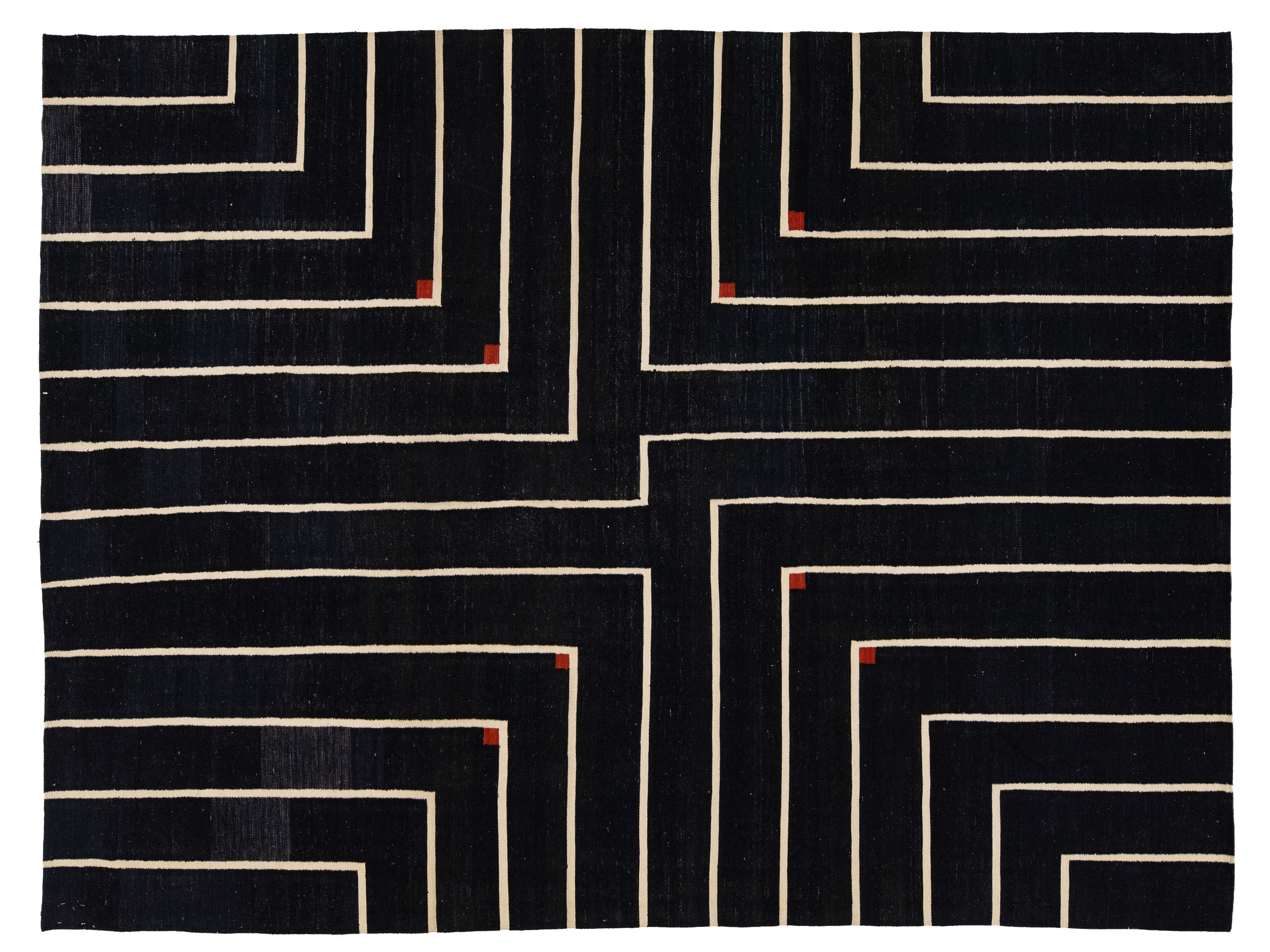 A rectangular black rug with a geometric maze-like pattern of cream lines and small red corner accents, shown flat against a white background.