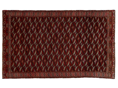 A rectangular traditional rug with a deep red field, featuring a repeating diamond pattern in cream, black, and red, and a detailed geometric border.