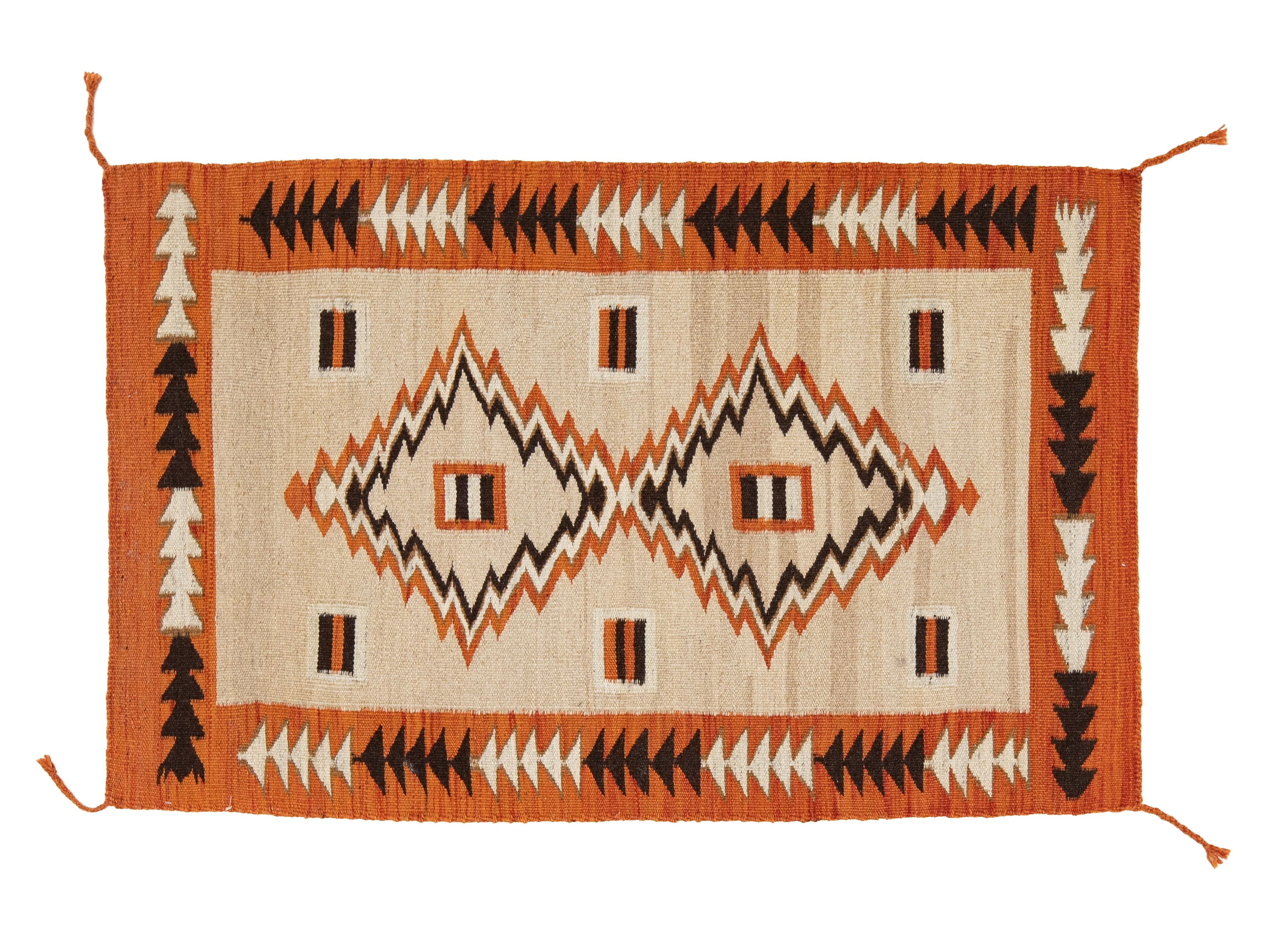 A rectangular woven rug with a Southwestern geometric pattern, featuring an orange border, a cream center, and black and orange zigzag diamond motifs.