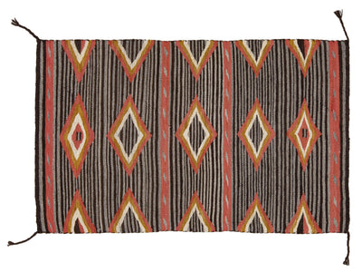 A rectangular woven rug with a Southwestern geometric pattern, featuring stripes and diamond motifs in brown, red, orange, cream, and black.
