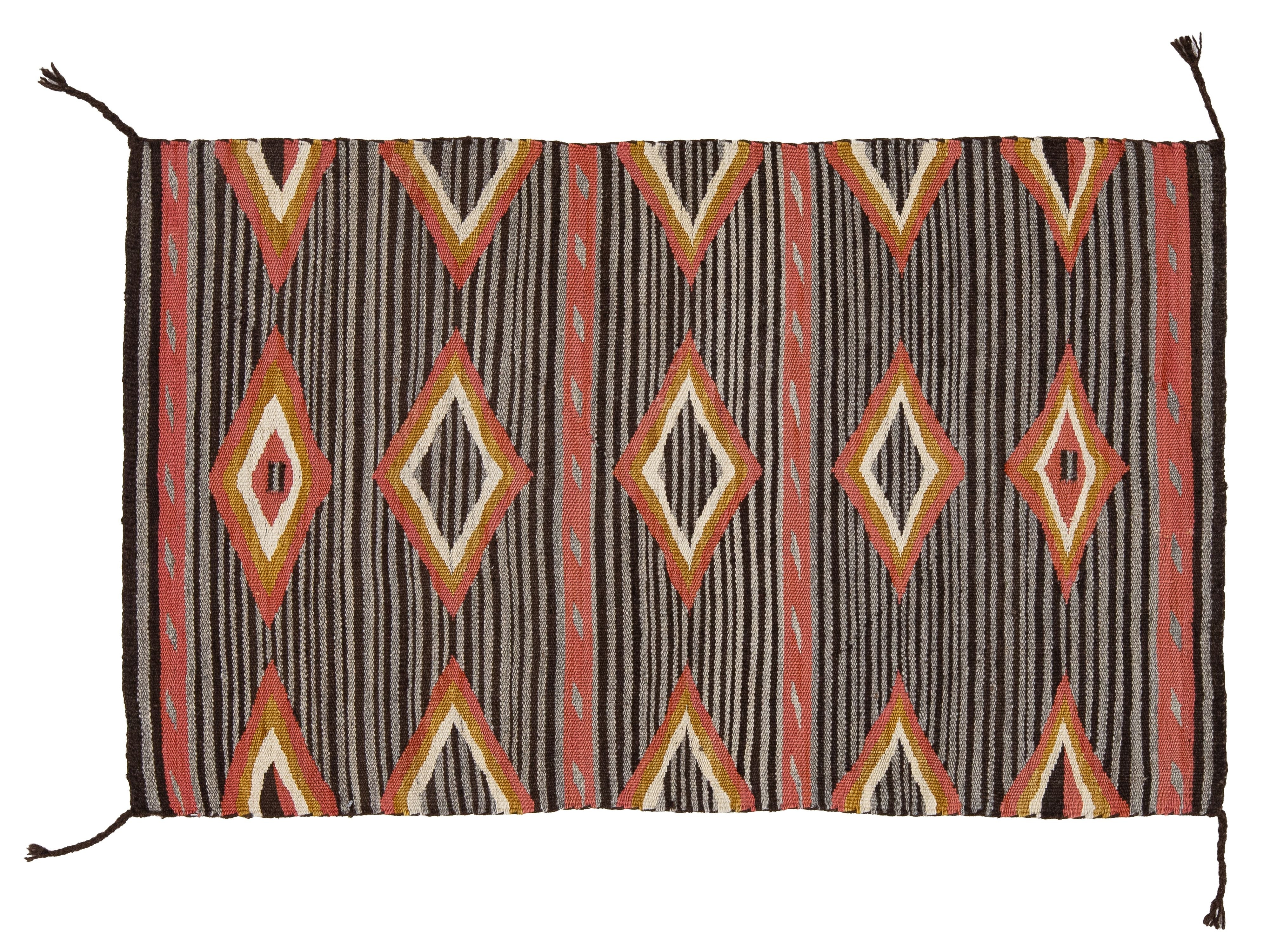 A rectangular woven rug with a Southwestern geometric pattern, featuring stripes and diamond motifs in brown, red, orange, cream, and black.