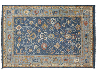 A traditional hand-knotted area rug with a navy blue central field, surrounded by a light blue border and a beige outer frame, featuring intricate floral and geometric motifs in cream, rust, and gold.