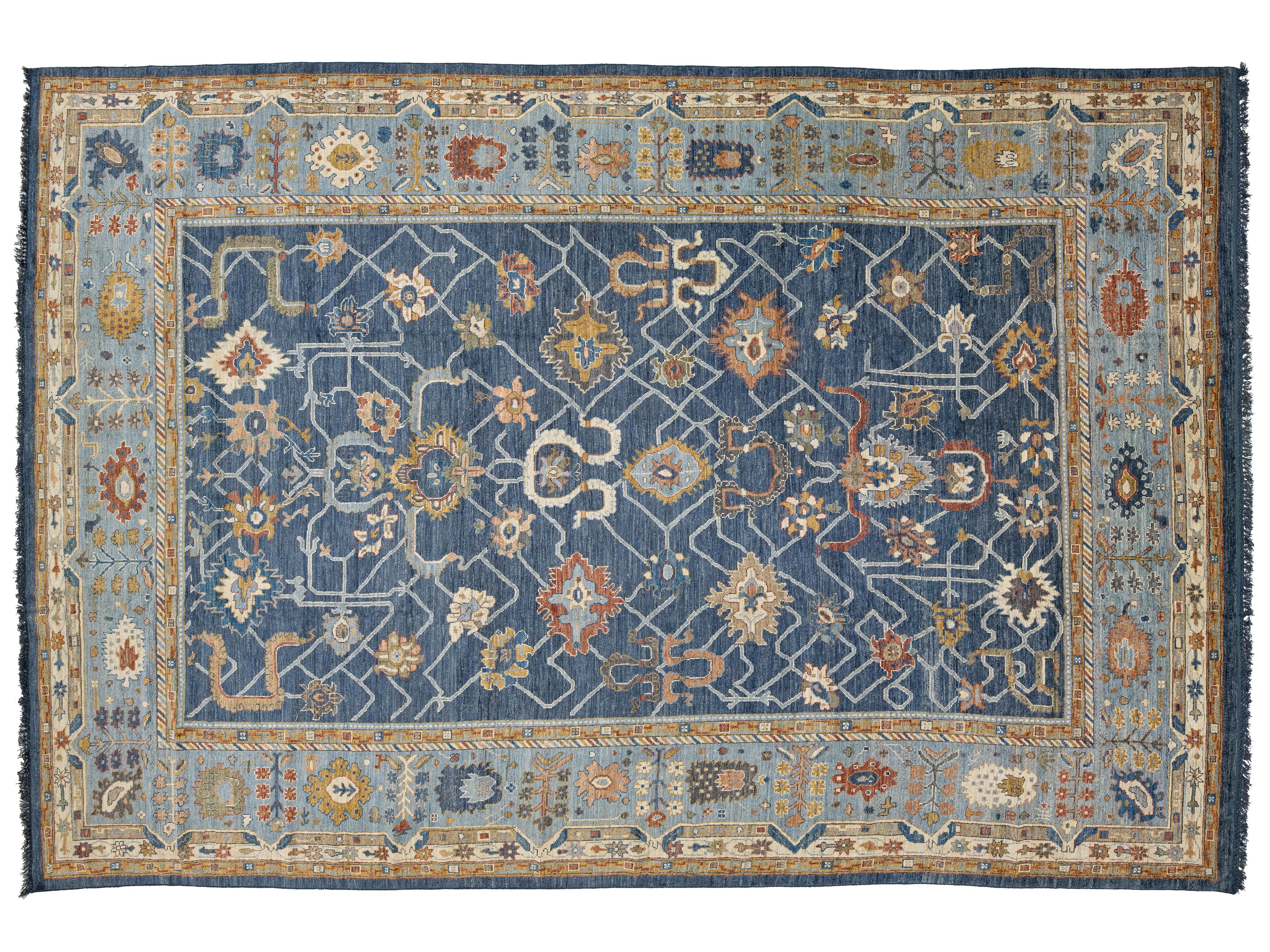 A traditional hand-knotted area rug with a navy blue central field, surrounded by a light blue border and a beige outer frame, featuring intricate floral and geometric motifs in cream, rust, and gold.