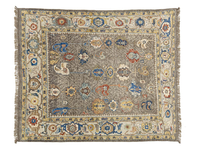 A rectangular oushak-style area rug with a distressed, faded pattern. The central field is a muted taupe-gray, surrounded by a cream-colored inner border and a wide outer border featuring traditional floral motifs in blue, rust red, and mustard yellow.