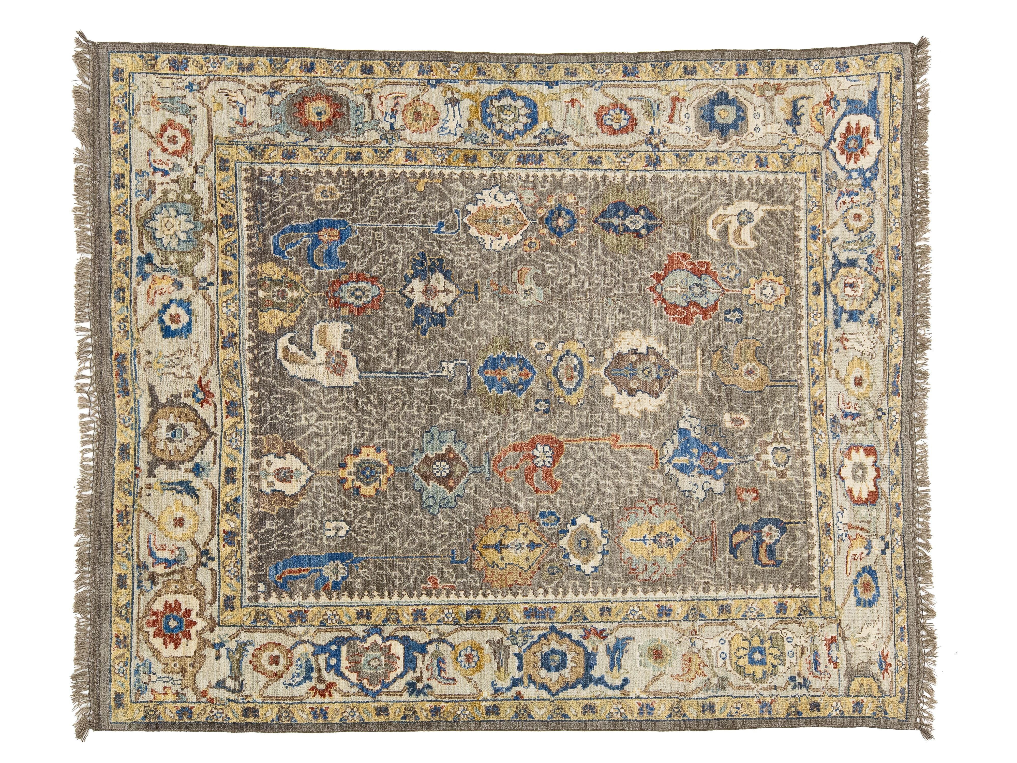A rectangular oushak-style area rug with a distressed, faded pattern. The central field is a muted taupe-gray, surrounded by a cream-colored inner border and a wide outer border featuring traditional floral motifs in blue, rust red, and mustard yellow.