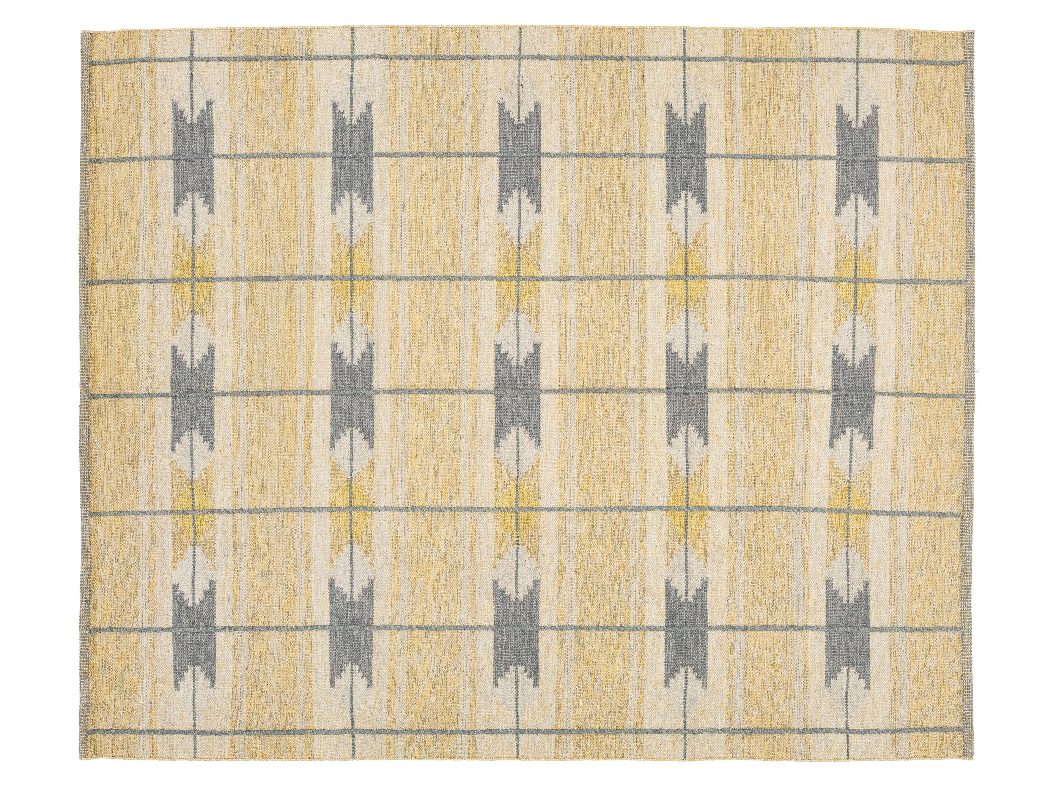 A rectangular area rug with a textured, woven pattern featuring vertical columns of gray and mustard yellow geometric motifs on a warm beige background, framed by thin gray horizontal and vertical lines.