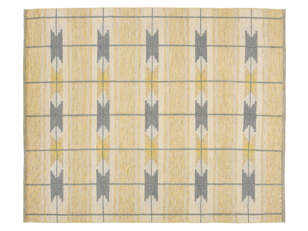 A rectangular area rug with a textured, woven pattern featuring vertical columns of gray and mustard yellow geometric motifs on a warm beige background, framed by thin gray horizontal and vertical lines.