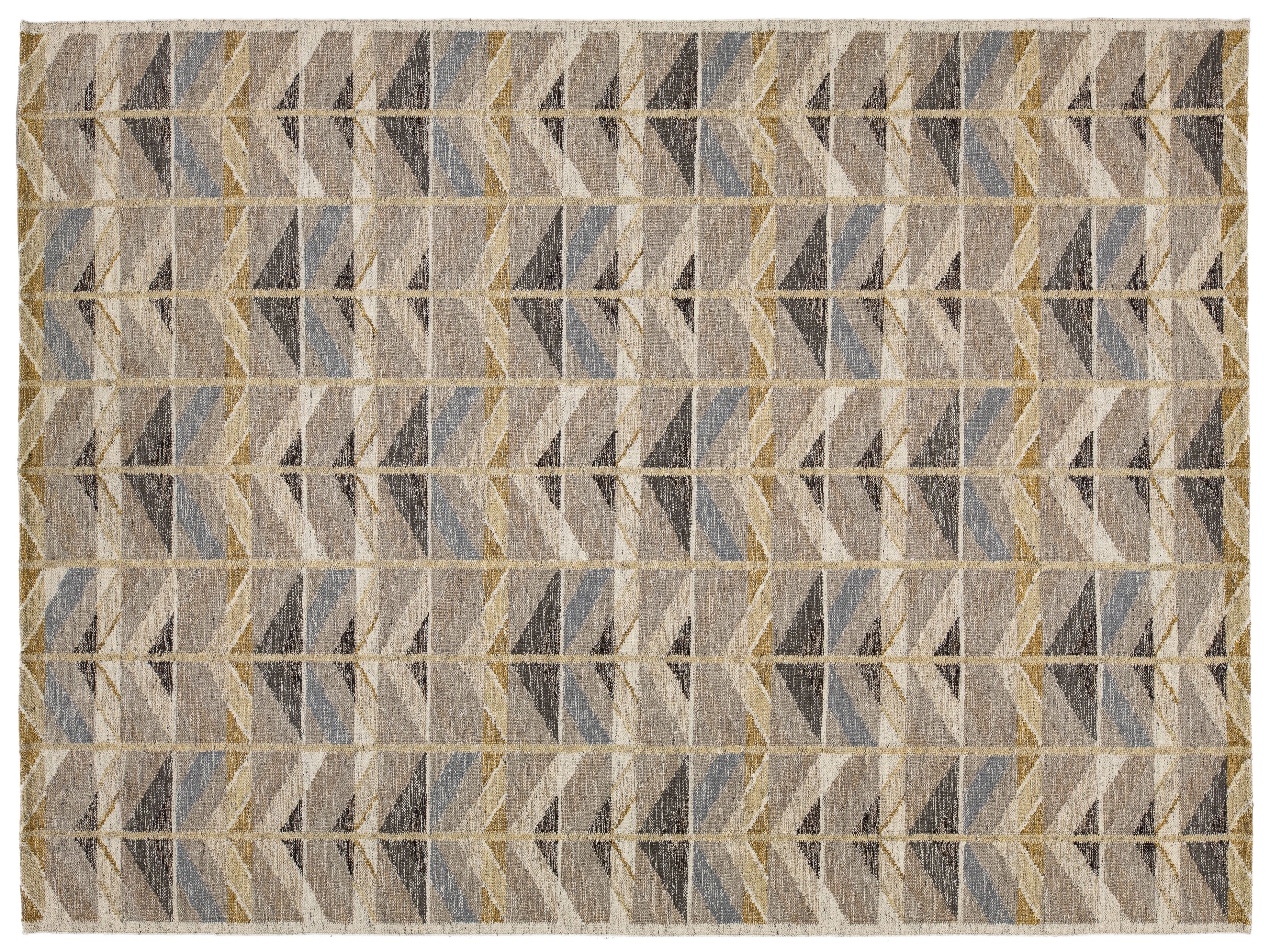 A rectangular area rug with a geometric chevron pattern in shades of beige, gray, brown, and muted blue, framed by a thin cream border.