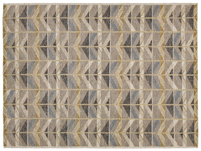 A rectangular area rug with a geometric chevron pattern in shades of beige, gray, brown, and muted blue, framed by a thin cream border.