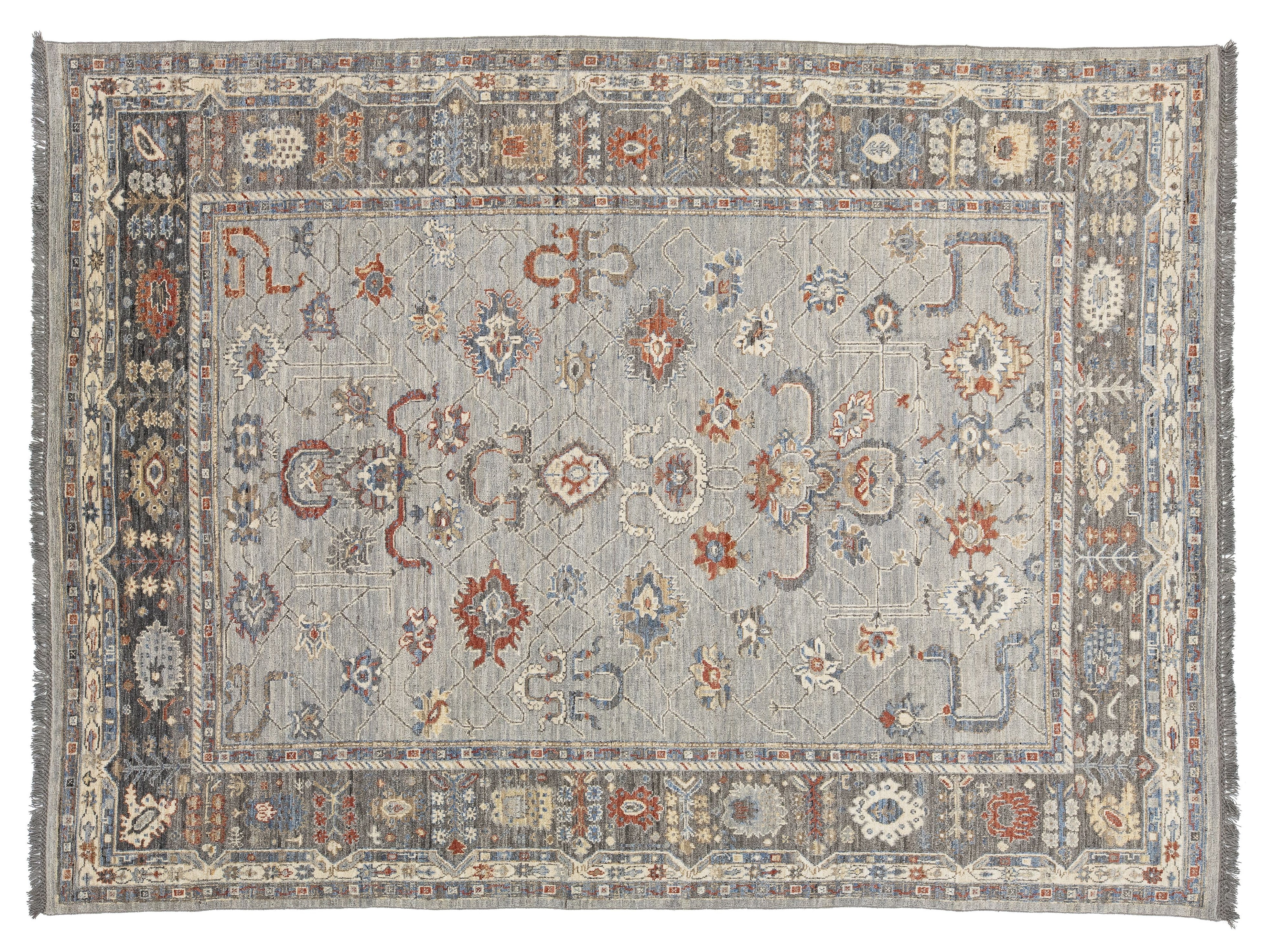 A rectangular oushak-style area rug with a distressed gray-blue field and an ornate multi-colored border featuring red, orange, cream, and blue motifs.
