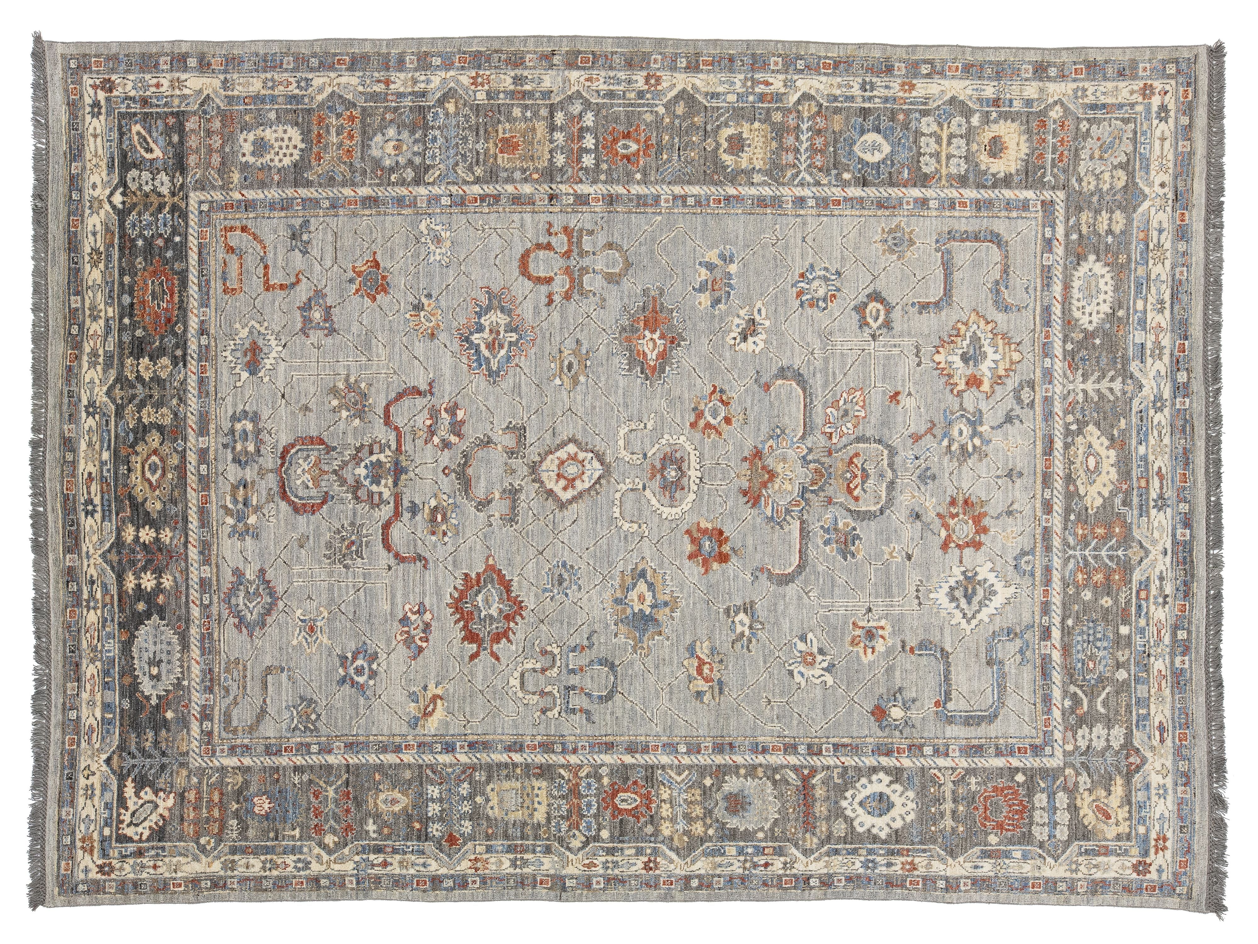 A rectangular oushak-style area rug with a distressed gray-blue field and an ornate multi-colored border featuring red, orange, cream, and blue motifs.