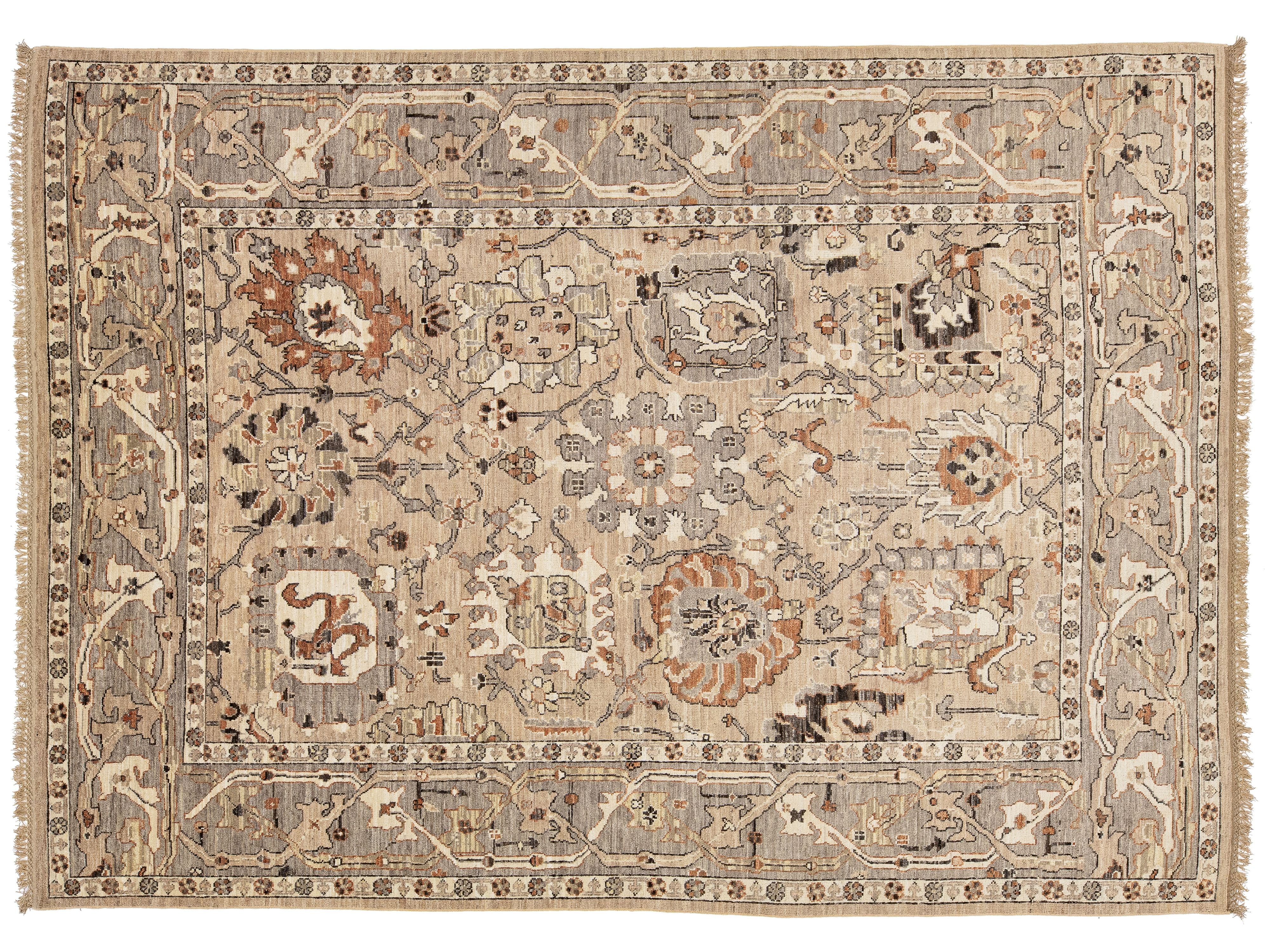 A traditional oushak-style area rug with an intricate floral and geometric pattern in beige, brown, and muted orange tones, featuring a central medallion and fringed edges.
