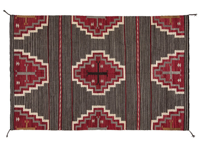 A rectangular woven rug with a Southwestern geometric pattern, featuring red and beige diamond medallions on a dark charcoal gray striped background.