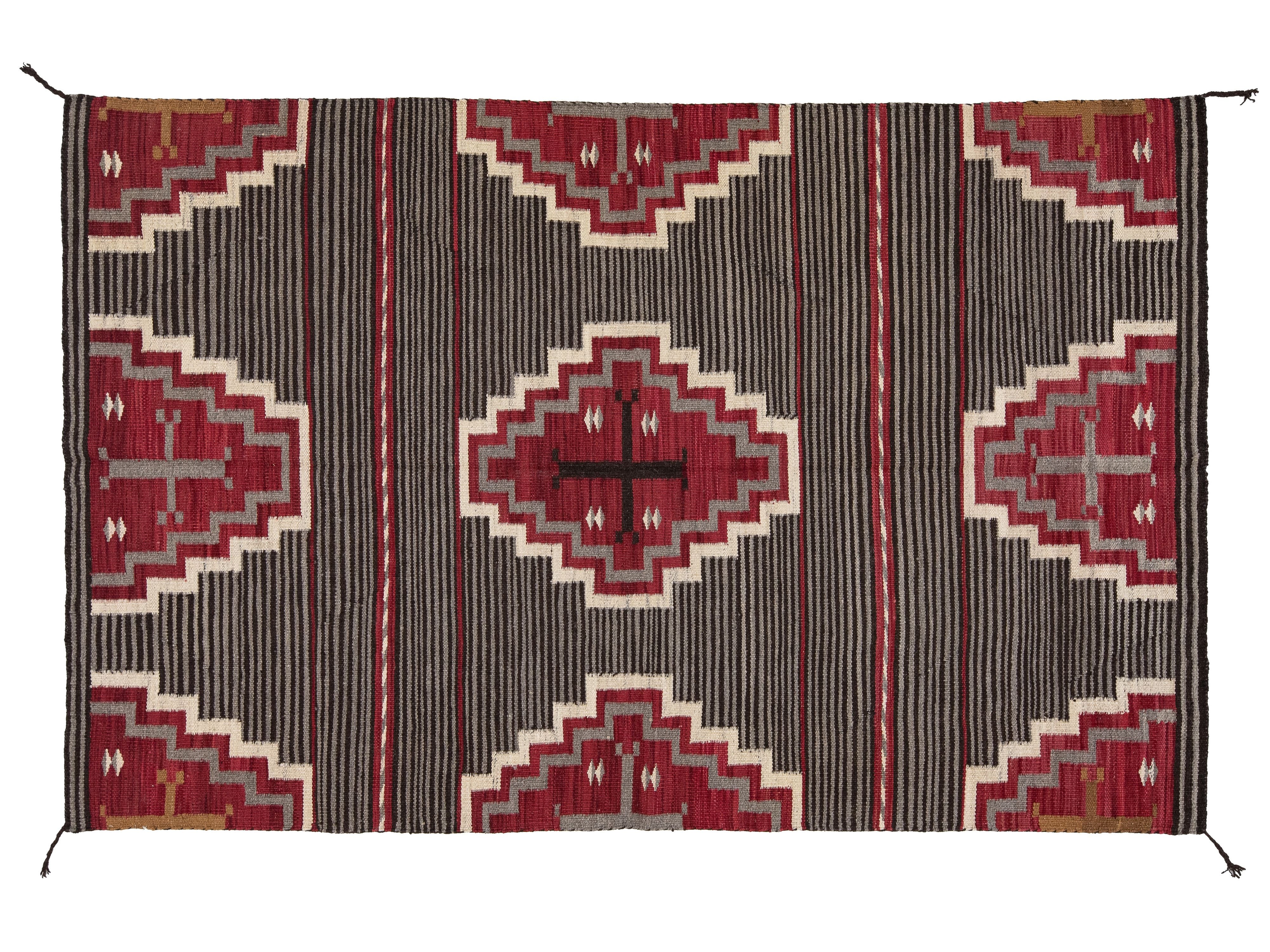 A rectangular woven rug with a Southwestern geometric pattern, featuring red and beige diamond medallions on a dark charcoal gray striped background.