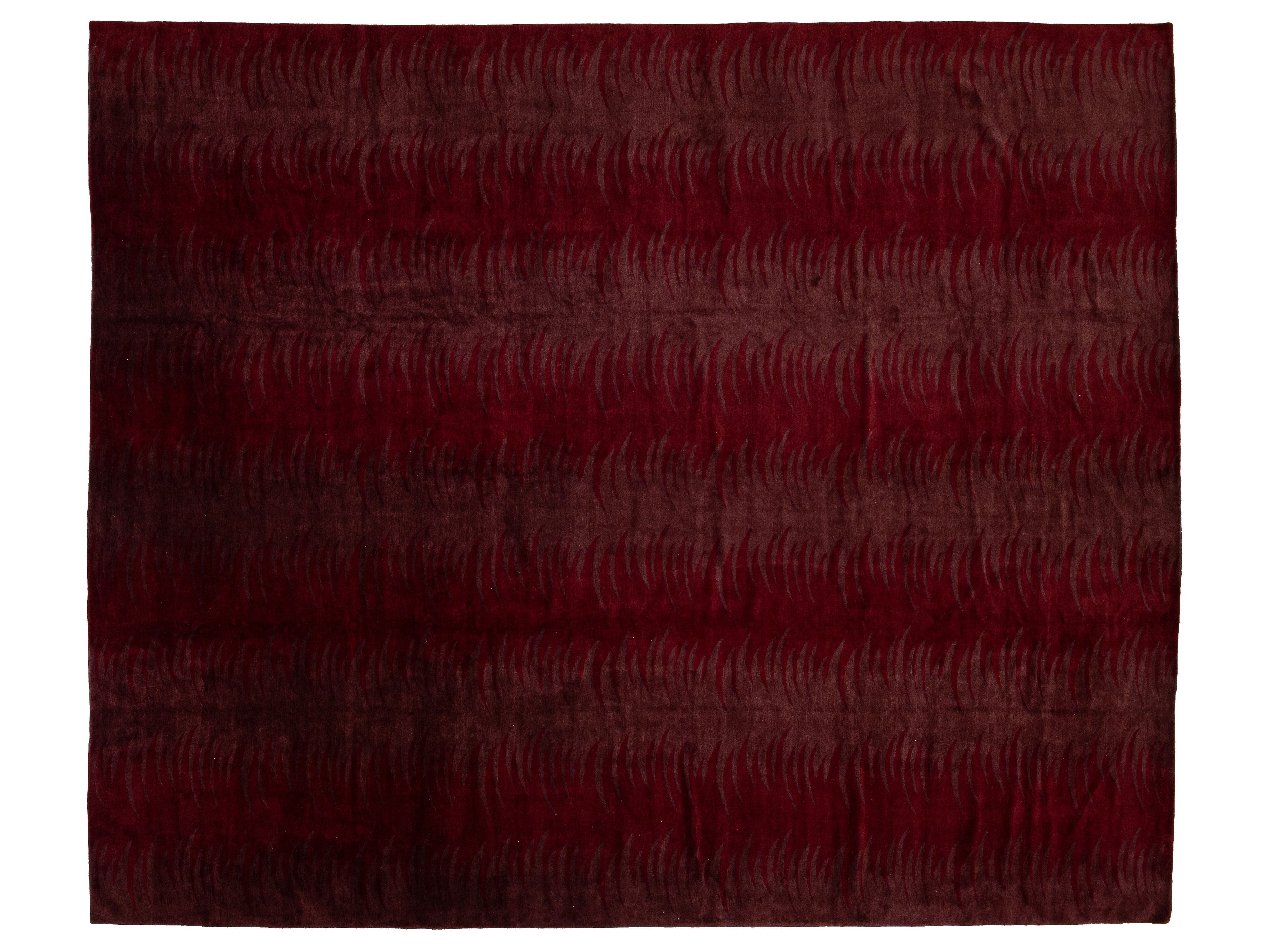 A rectangular area rug with a deep burgundy and dark red abstract pattern of wavy lines, shown flat against a white background.