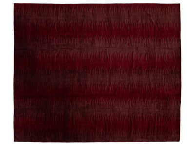A rectangular area rug with a deep burgundy and dark red abstract pattern of wavy lines, shown flat against a white background.
