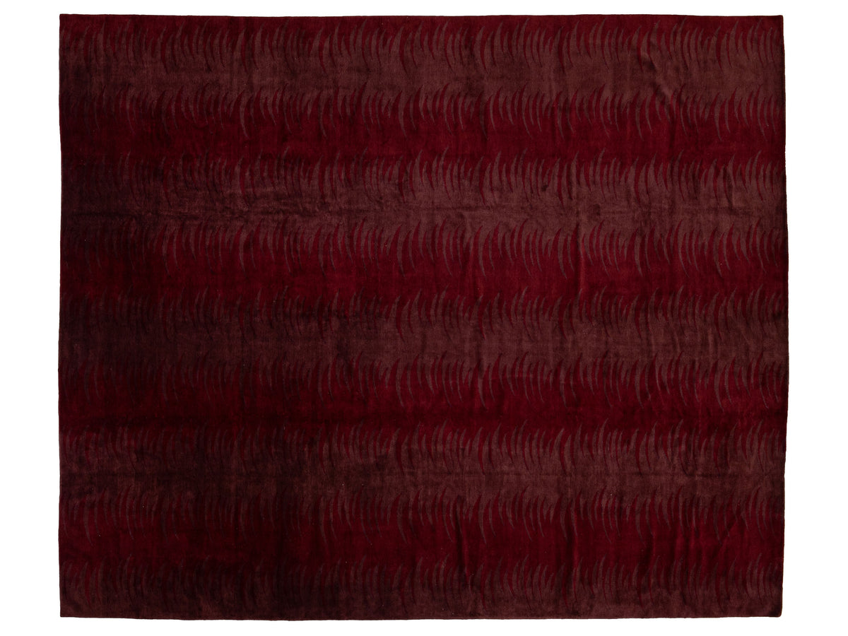 A rectangular area rug with a deep burgundy and dark red abstract pattern of wavy lines, shown flat against a white background.