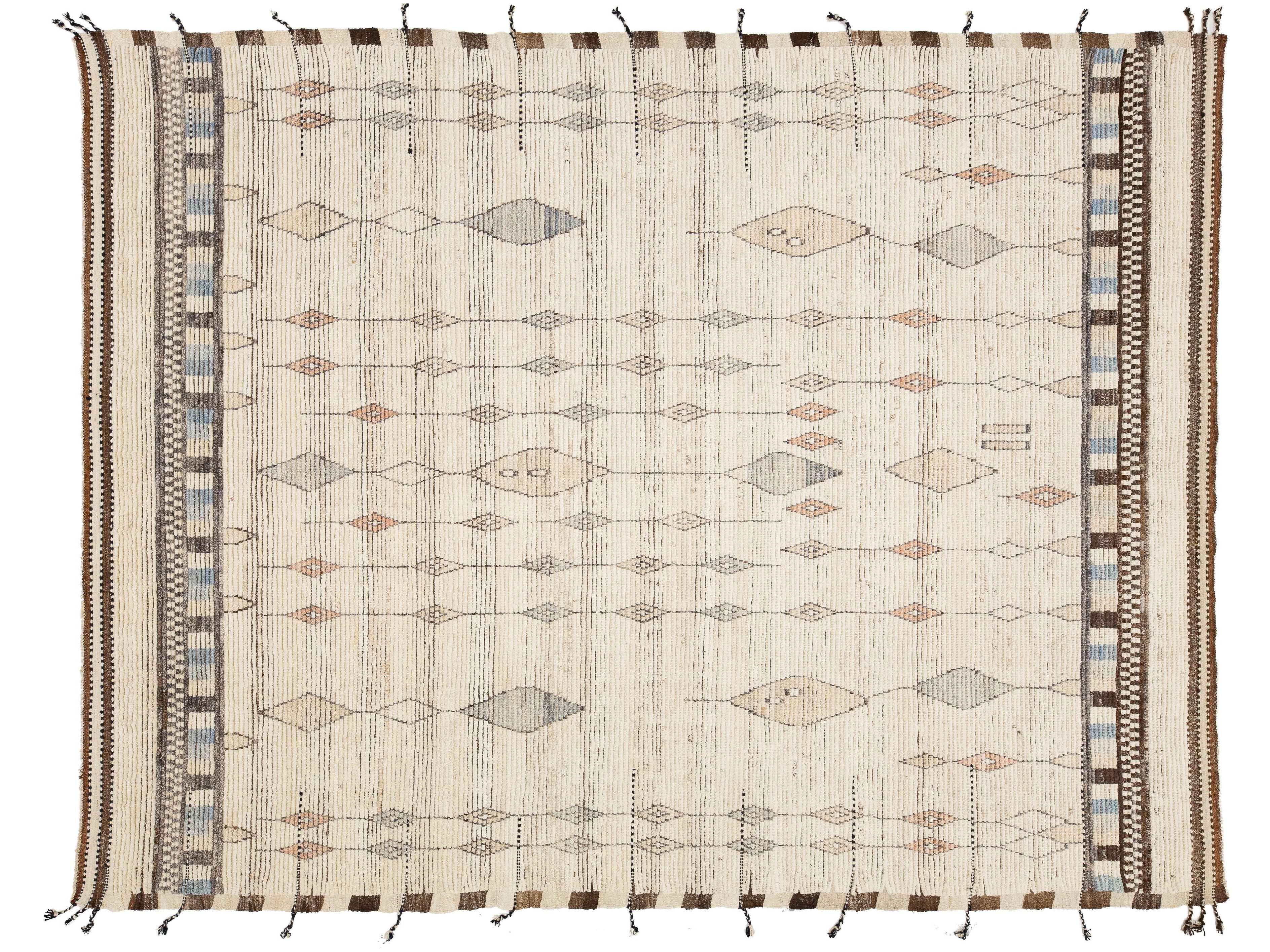 A rectangular woven rug with a cream base and geometric diamond motifs in muted brown, beige, gray, and blue, finished with fringe tassels on the sides.