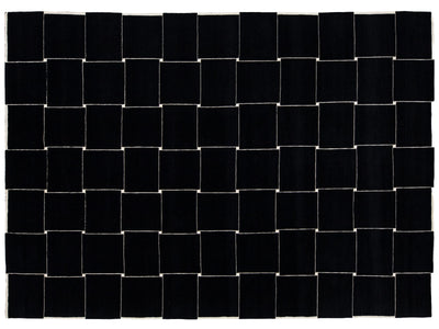 A rectangular black woven rug with a geometric basketweave pattern created by alternating black and off-white woven squares.
