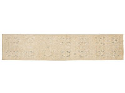 A runner rug in a light beige or cream tone with a faded, distressed pattern of muted blue and gray motifs.