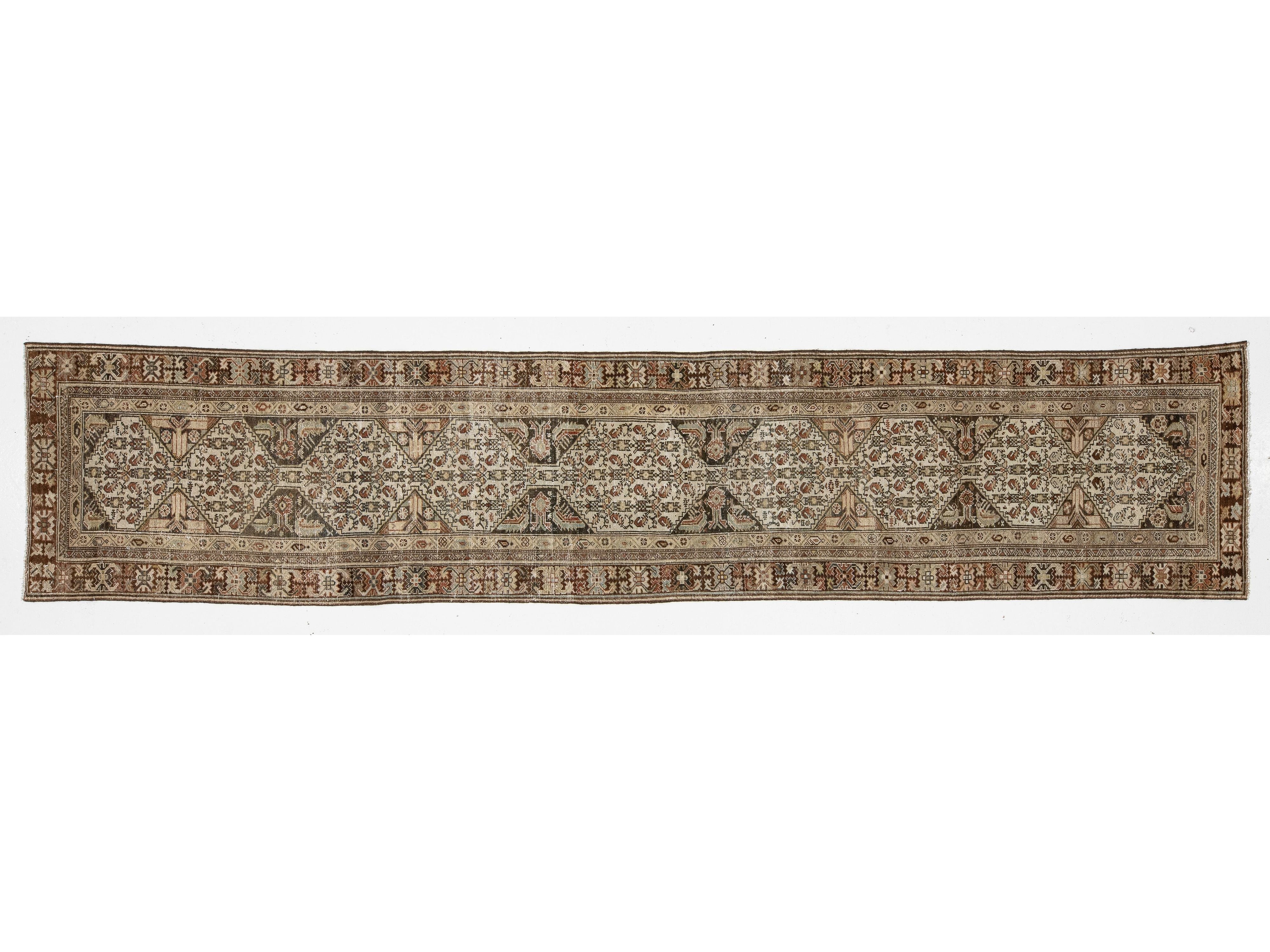 A long rectangular area rug with an intricate traditional floral and geometric pattern in beige, brown, and muted blue tones, shown flat against a white background.