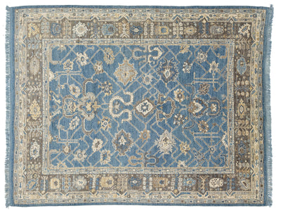 A rectangular traditional area rug with an intricate floral and geometric pattern, featuring a dominant medium blue center field, a beige and brown border, and blue fringe on the sides.