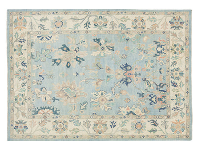 A rectangular area rug with an intricate floral and botanical pattern, featuring a light blue center field and a cream border with blue, green, and peach details.