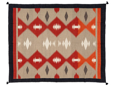A rectangular rug with a Southwestern geometric pattern, featuring red and orange diamonds, white and gray accents, and a dark navy border.